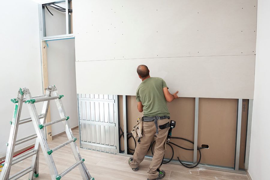 um trabalhador aplicando com facilidade o gesso acartonado em uma parede do edifício 