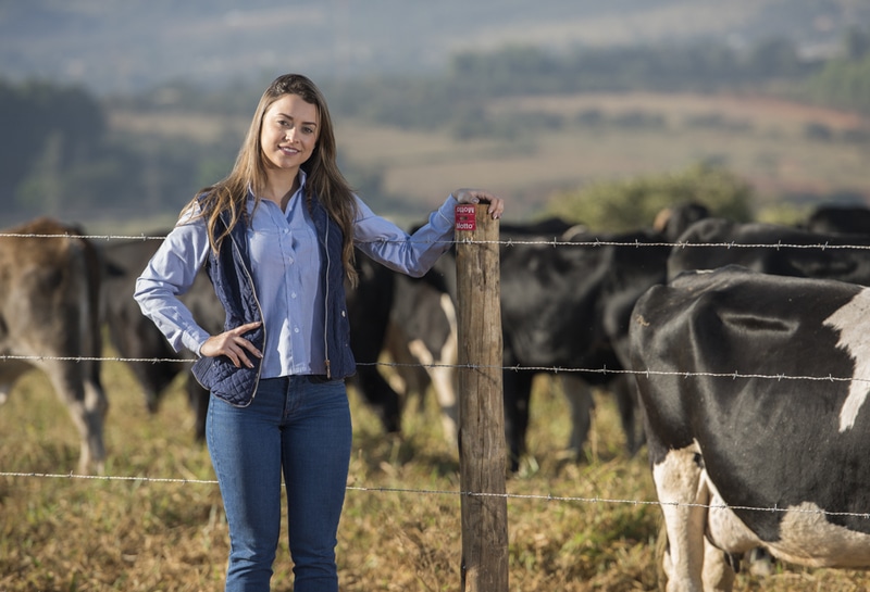 Mulher posando para fotografia com cerca e vacas leiteiras ao fundo